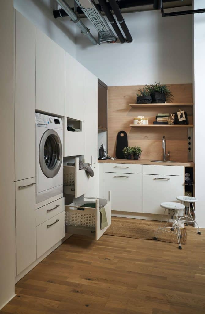 Une buanderie blanche avec une machine à laver en hauteur et des tiroirs de rangements ouverts